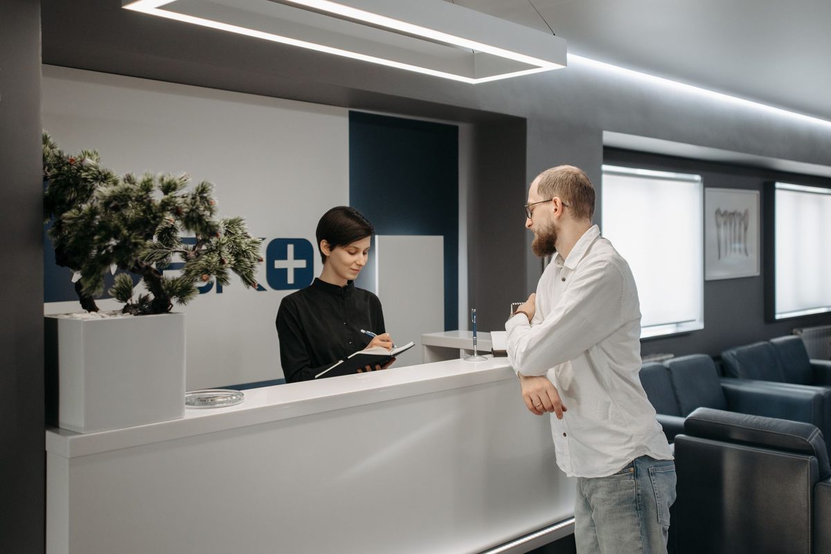 A staff member assisting a patient at a clinic reception desk